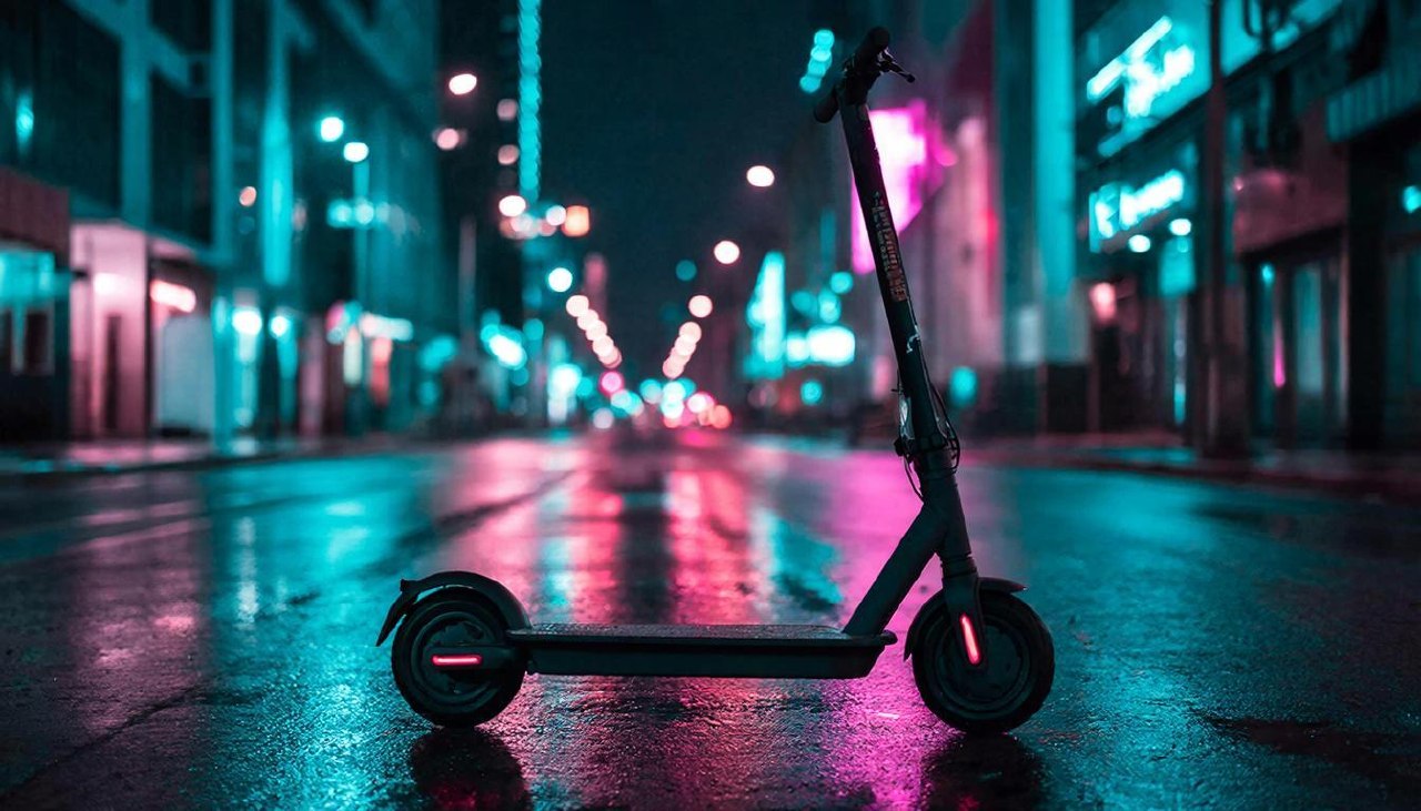 Современный самокат на ночной улице под неоновым светом.